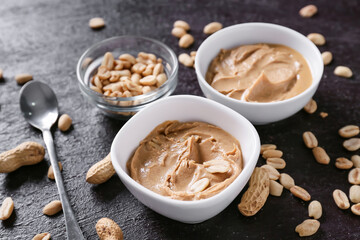 Bowls with tasty peanut butter on dark background