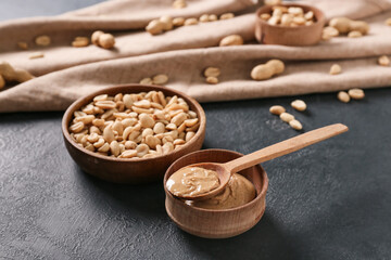 Fototapeta na wymiar Bowls with tasty peanut butter and nuts on color background
