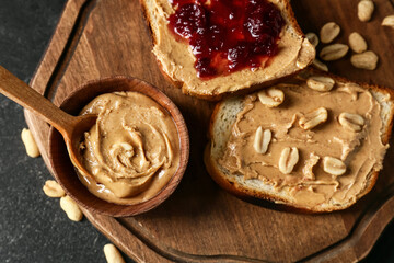 Board with tasty peanut butter and bread on dark background