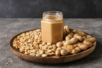 Jar with tasty peanut butter and nuts on grunge background
