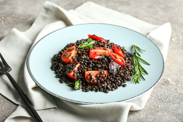 Plate with tasty cooked lentils and vegetables on grunge background