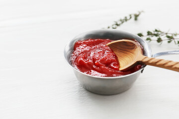 Pot and spoon with tasty barbecue sauce on light wooden background