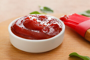 Bowl with tasty barbecue sauce and silicone brush on wooden background