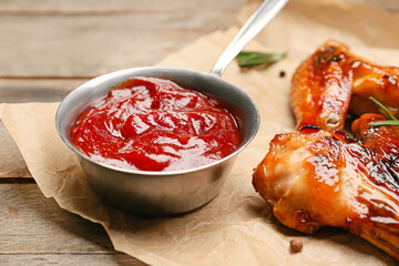 Chicken wings and pot with barbecue sauce on wooden background