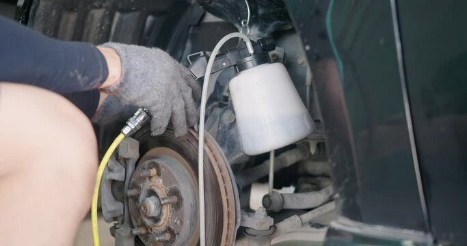 Auto mechanic replacing brake fluid on a vehicle, technician bleed air out of disc brake system in garage workshop, Car repair in a car service