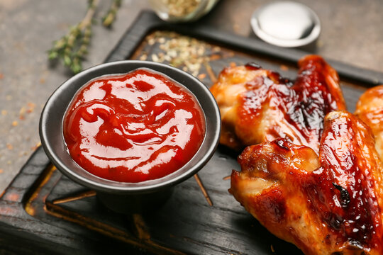 Board with roasted chicken wings and barbecue sauce on grunge background