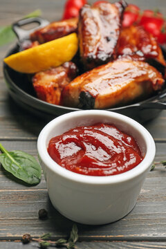 Bowl with tasty barbecue sauce and roasted pork on wooden background