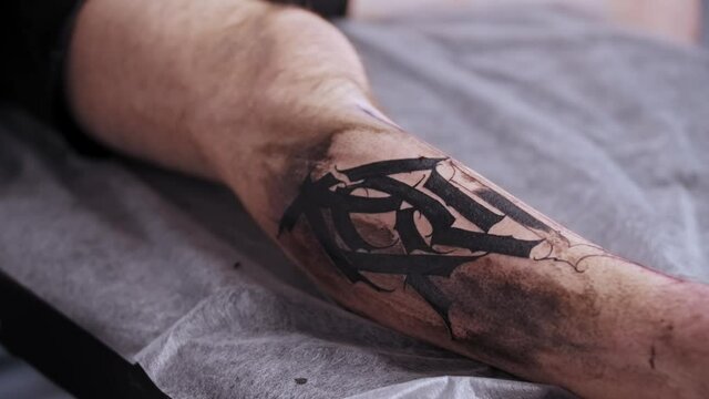 A session in tattoo salon - filling in the tattoo with solid black color in letters
