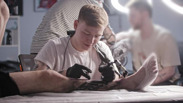 A session at the tattoo salon - young man master tattooing big letters on the leg