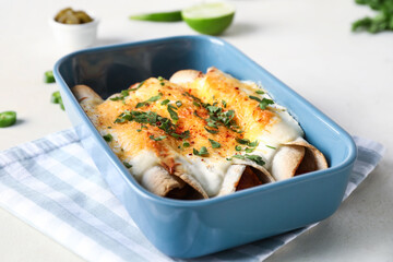Baking dish with tasty cooked enchilada on table