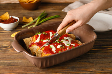 Woman cutting hot enchilada in baking dish on table