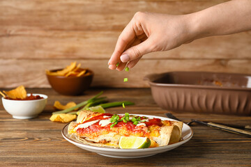 Woman adding green onion to tasty enchilada on plate