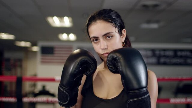 Portrait Of Beautiful Young Tired And Sweaty Woman Boxer Turning Face To Camera With Serious Look At Dark Ring.