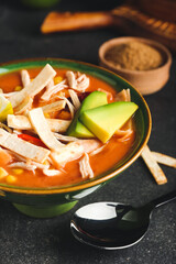 Bowl of tasty chicken enchilada soup on dark background