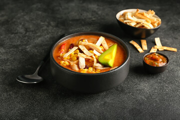 Bowl of tasty chicken enchilada soup on dark background