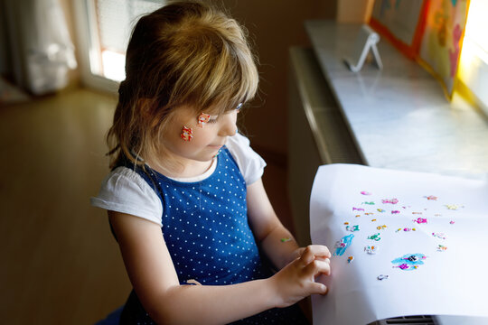 Little toddler girl playing with different colorful animal stickers. Concept of activity of children during pandemic corona virus quarantine. Happy funny child having fun with stick stickers on face.