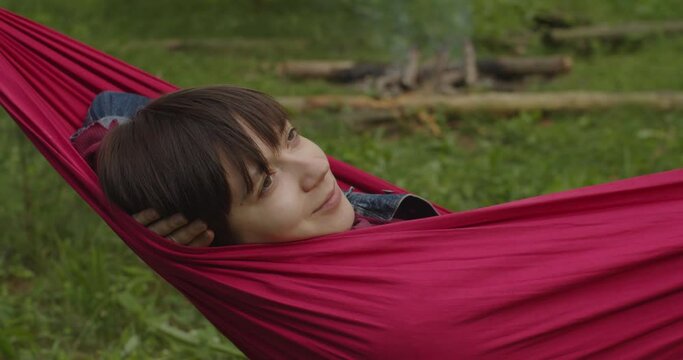 Crop zooming shot of young woman having rest napping in hammock in summer green forest. Young girl on a camping trip relaxes on her hammock. Leisure travel adventure camping equipment 