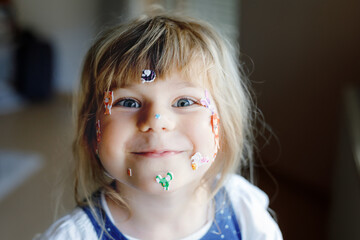 Little toddler girl playing with different colorful animal stickers. Concept of activity of children during pandemic corona virus quarantine. Happy funny child having fun with stick stickers on face.