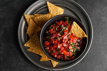 Bowl of tasty Pico de Gallo salsa and nachos on dark background