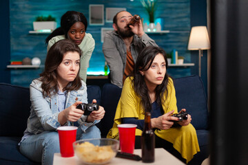 Multi ethinc friends cheerful group of people relaxing on console games with controller. Group of mixed race friends playing games while sitting on sofa in living room late at night.