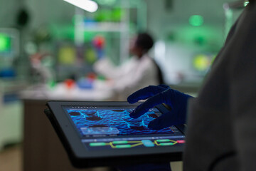 Scientist researcher doctor analyzing genetic mutation test using tablet while her collegue typing...