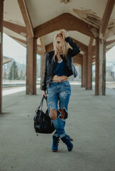 Vertical shot of a sexy Bosnian blonde woman with tall blue boots under an old building