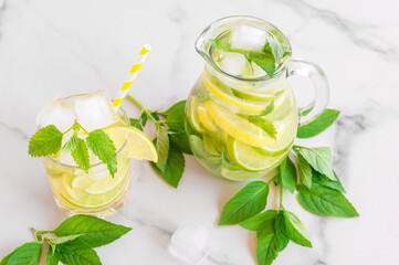 Summer refreshing detox cocktail. Water with lemon, mint and ice in mason jar on white marble background. Rustic style.