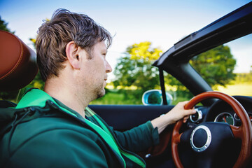 Happy young man driving a cabriolet car on sunny summer day. Sunset, happiness, freedom