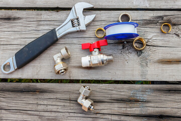 Various plumbing spare parts, sealing tape and adjustable wrench on rustic wooden background. Top view