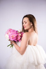 Beautiful cheerful young blonde girl wearing dress standing isolated over white background, holding bouquet of peonies