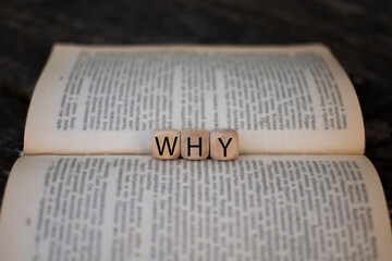 the word why on the wooden cubes on the background of the book pages. FAQ frequency asked...