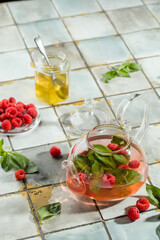 Hot raspberry tea in transparent teapot on a stone table. Fresh berries, mint, glass cup