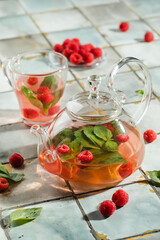 Hot raspberry tea in transparent teapot on a stone table. Fresh berries, mint, glass cup
