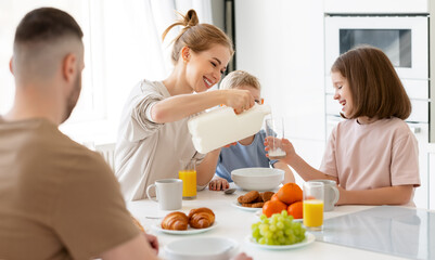 Young happy family with two cute little kids having breakfast together in kitchen and smiling