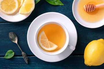 A cup of lemon tea with honey, shot from the top on a dark rustic wooden background. Healthy organic citrus warm beverage