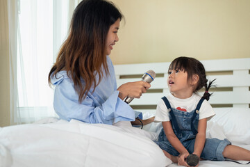 Fototapeta premium Happy Asian family loving children, kid and her sister holding microphone and singing together on bed in bedroom