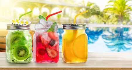 Fototapeta na wymiar Summer refreshing exotic drinks cocktails in glass jars with straws on wooden counter on swiming pool background.