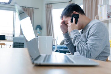 A young businessman use mobile and laptop sitting at wooden table at home, freelancer working on notebook.