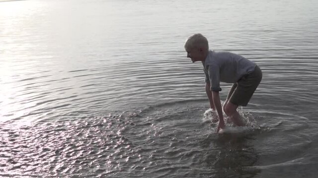 A boy splashes water in a lake at sunset. Beautiful light, slow motion.