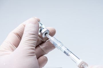 Doctor hand wears white medical glove holding flu, covid-19 liquid vaccine vial bottle and syringe are filling for preparing injection. Vaccination for fight Covid-19 virus concept.
