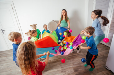 Fototapeta premium Schoolchildren playing using parachute with friends in gym