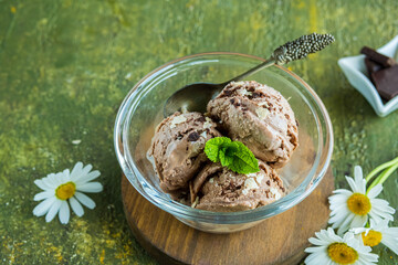 Three scoops of homemade chocolate ice cream in a glass bowl on a green concrete background