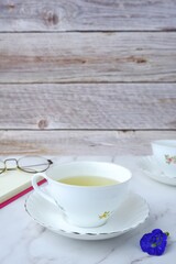 tea mug with glasses and a notebook with a pen rests on a marble table with a wooden background