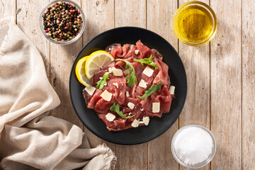 Marbled beef carpaccio on black plate and rustic wooden table. Top view. 