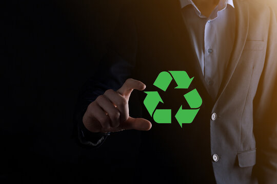 Businessman in suit over dark background holds an recycling icon, sign in his hands. Ecology, environment and conservation concept. Neon red blue light