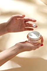 Poster beauty product, cosmetics and people concept - female hand holding jar of moisturizer on beige background © Syda Productions