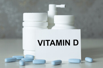 white card with text VITAMIN D on a table next to jars of medicine and pills are scattered on the table in front of the card, medical concept