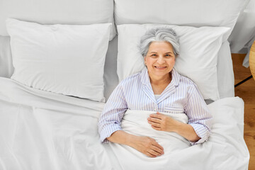 sleeping, old age and people concept - happy smiling awake senior woman lying in bed at home bedroom