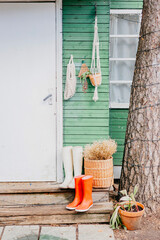 porch of a rustic wooden village house in white and green color with rubber boots at the doorstep,...