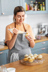 culinary, bake and cooking food concept - happy smiling young woman with baking bag making cupcake...